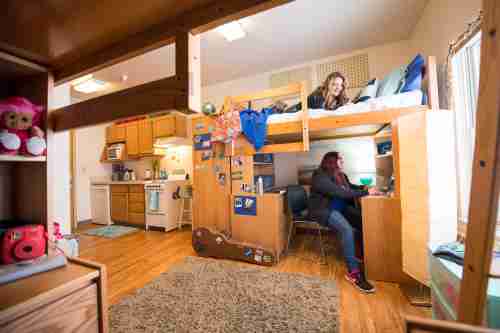 Two students talk in their dorm room. A kitchenette is in the background.
